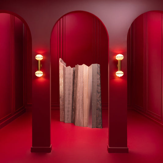 A dramatic interior scene with three red arched doorways framing a textured gray fabric curtain in the center. Red wall sconces glow on either side, and the entire space is bathed in deep red light.