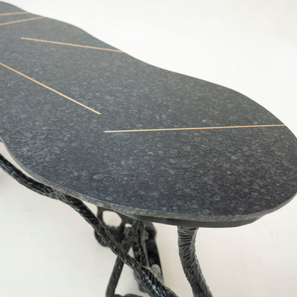 A close-up of a dark gray speckled stone or concrete board with thin gold linear accents, supported by twisted black cords, on a plain white background.